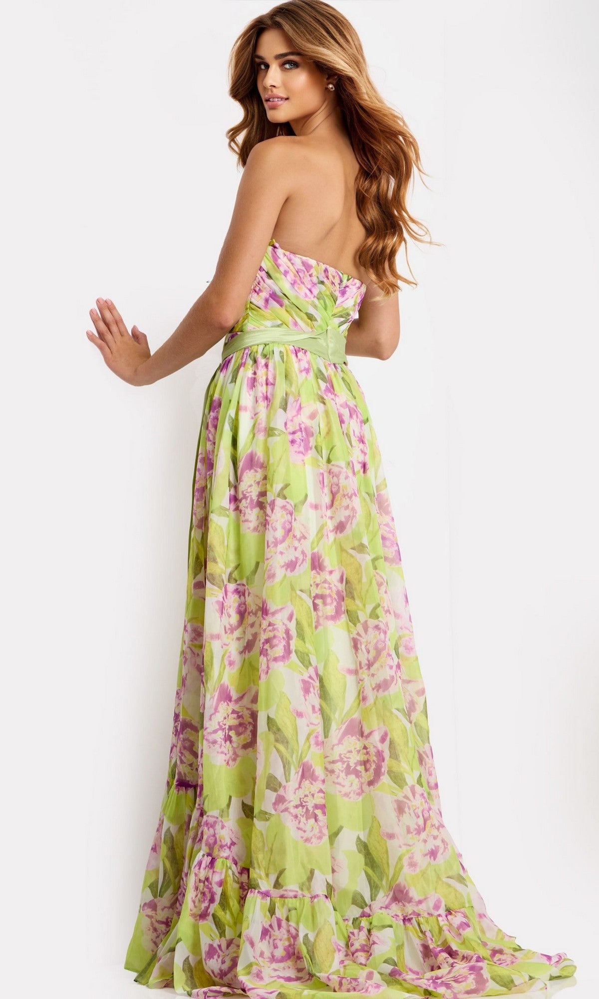 A woman stands with her back to the camera against a plain white background, wearing the Jovani 48468 long prom dress with a strapless green and pink floral print.